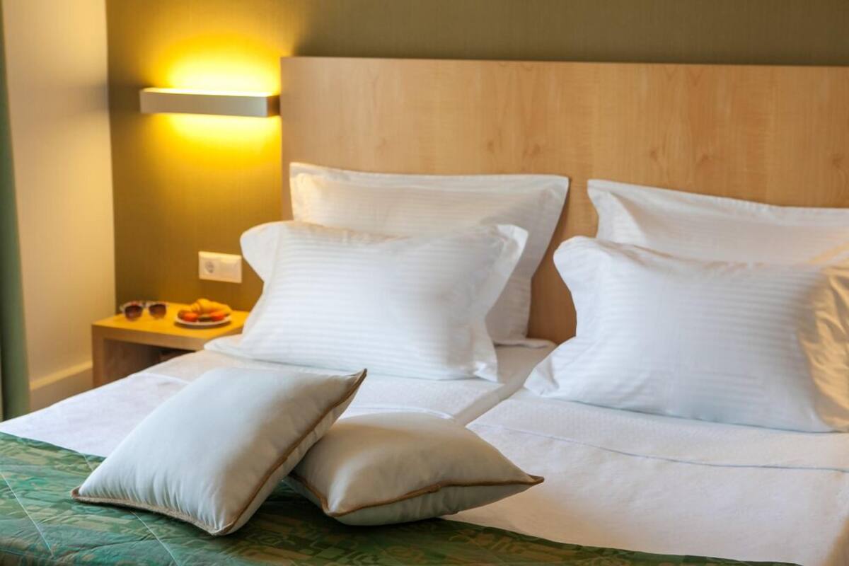 A hotel room with a wooden headboard, a bedside table with a lamp, and a bed with white bedding and pillows.