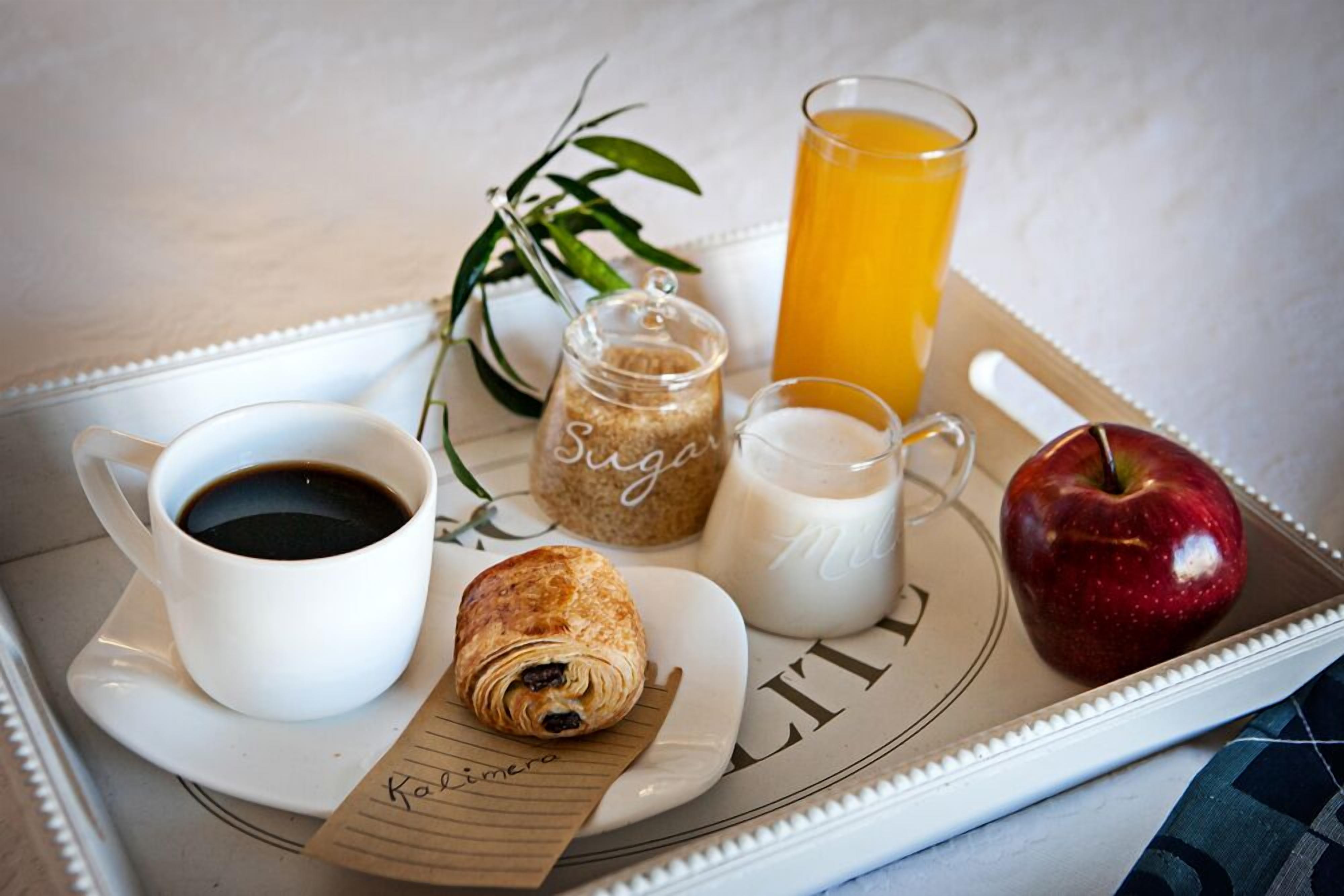 A tray with a croissant, a cup of coffee, a glass of orange juice, a jar of sugar, a glass of milk, and an apple.