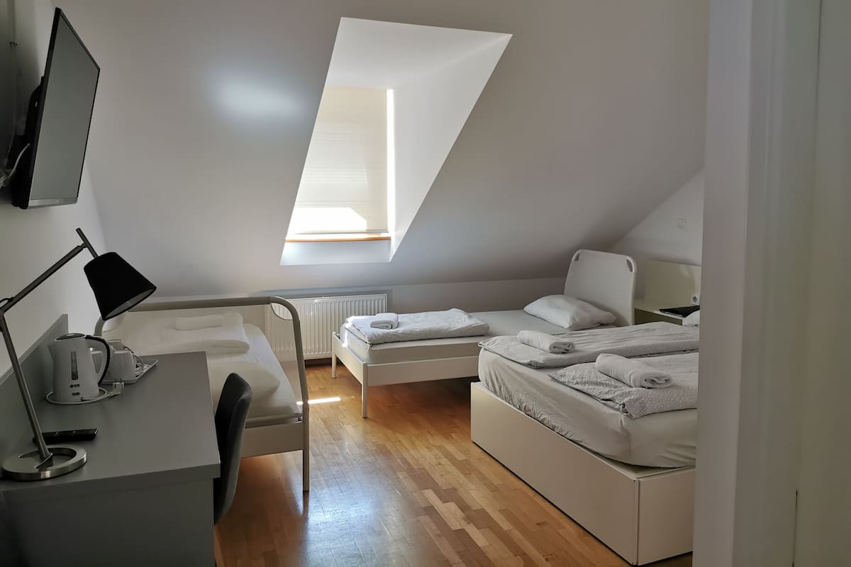 Une pièce moderne et bien éclairée, avec un plafond en pente, un bureau avec une lampe, deux lits et un radiateur.