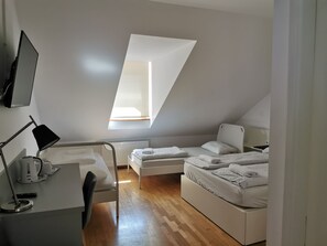 Een moderne, goed verlichte kamer met een schuine kap, een bureau met lamp, twee bedden en een radiator.
