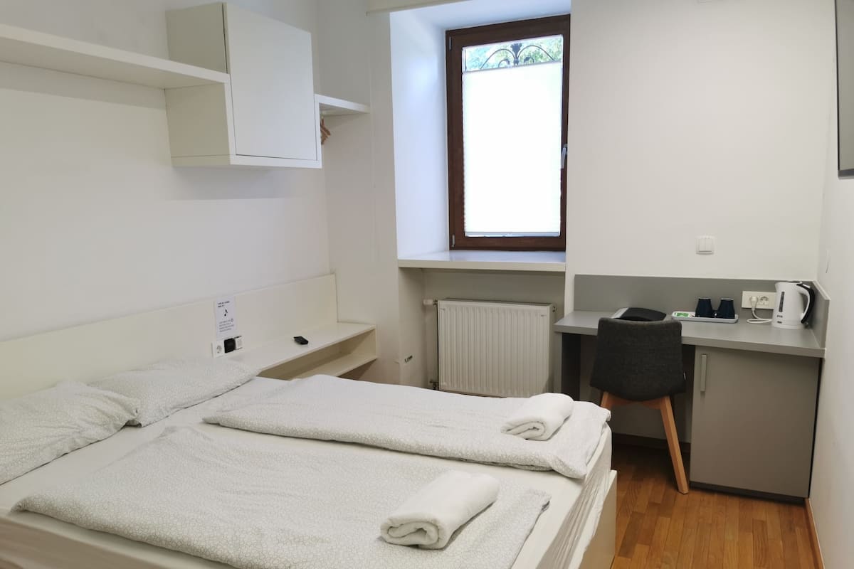 Une petite pièce propre, avec deux lits, un bureau, une chaise et une fenêtre.