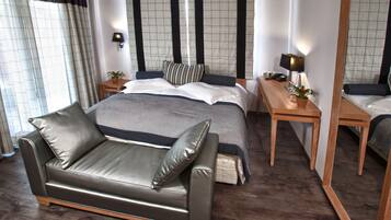 Un dormitorio moderno con una cama grande, un sofá de cuero, una mesita de noche con lámpara y un espejo.
