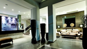 Een moderne lobby met een grote flatscreen televisie, een trap, een bank en hoge, zwarte kolommen.