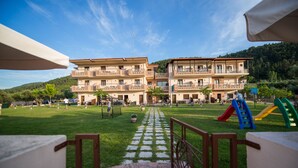 Un patio de hotel con un parque infantil, una cancha de tenis y un edificio con varios balcones.