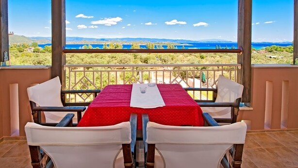 Un comedor con una mesa preparada para dos, con vistas a un paisaje pintoresco con colinas y una masa de agua.