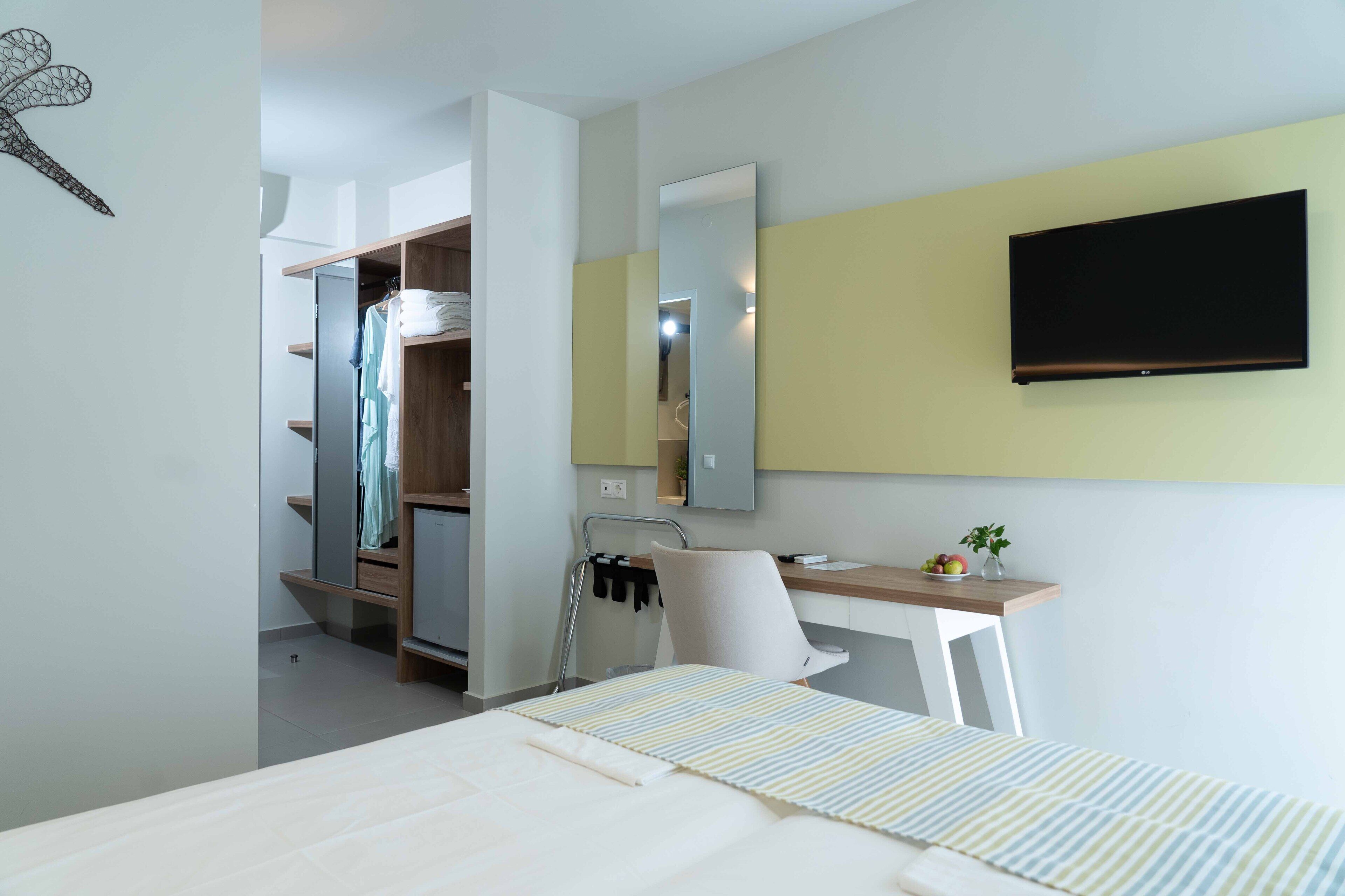 Une chambre d’hôtel équipée d’un lit, d’un bureau, d’une chaise, d’une télévision, d’une armoire et d’un miroir.