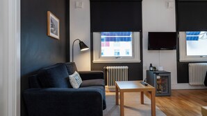 Una sala de estar moderna con un sofá, una mesa, una lámpara, un televisor y un mini refrigerador.