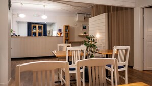 Un comedor con mesas de madera y sillas blancas, una barra con cortina azul, y una planta sobre la mesa.