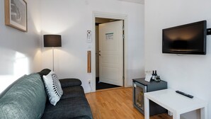 Un salón moderno con un sofá gris, una lámpara de pie, un televisor de pantalla plana y una mesita con botellas.