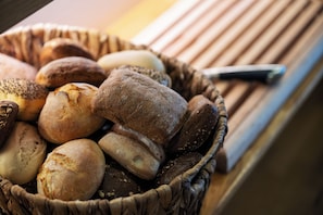 A basket of various breads and a knife on a wooden surface. - Port Hotel (Karlshamn)