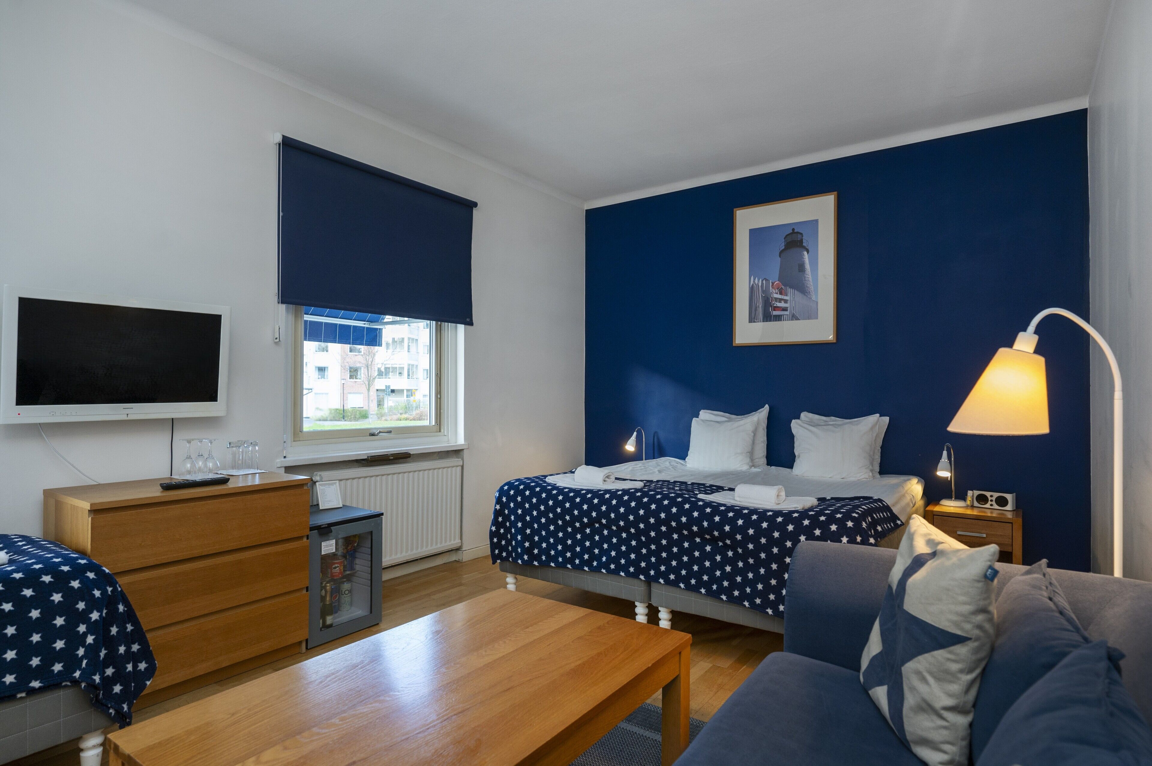 A hotel room with a bed, a desk, a television, a window with a view, and a nightstand with a lamp.