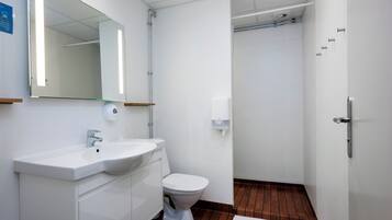 Et moderne badeværelse med hvid vask, spejl og toilet, trægulv samt et hvidt håndklæde på gulvet.
