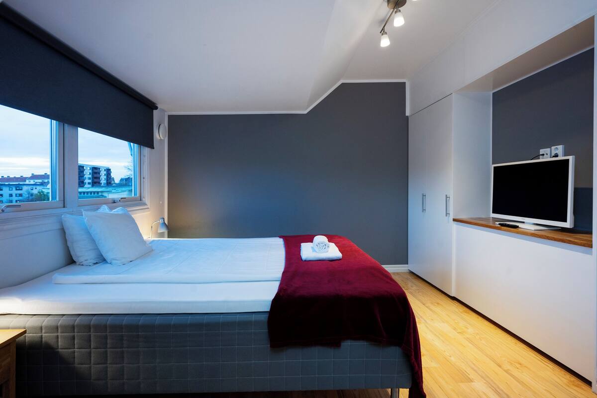 A modern hotel room with a large bed, a TV, and a window with a city view.
