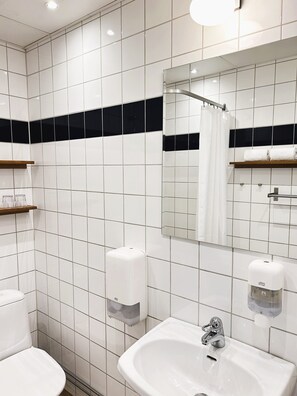 A modern bathroom with white tiles, a sink, a mirror, and a shower curtain. - Port Hotel (Karlshamn)