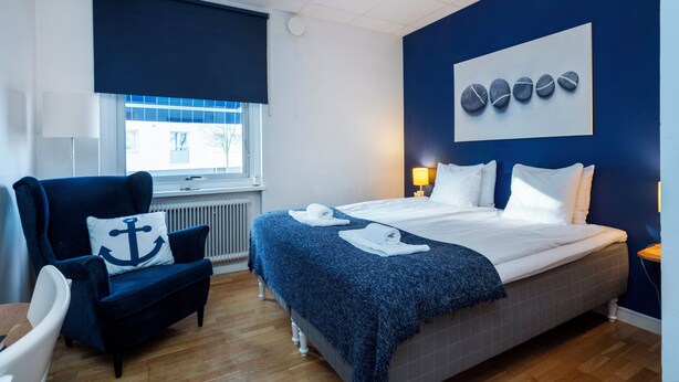 Una habitación de hotel con cama, una silla, un ventanal y una pared decorada con un cuadro.