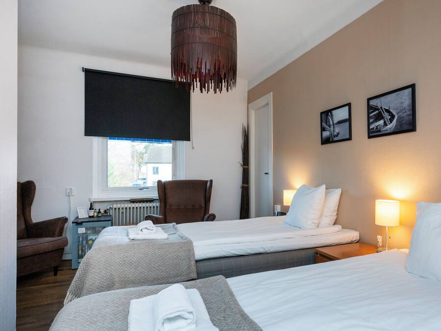 Une chambre d’hôtel avec deux lits, une chaise, un bureau avec un ordinateur, un radiateur et une fenêtre avec des stores.