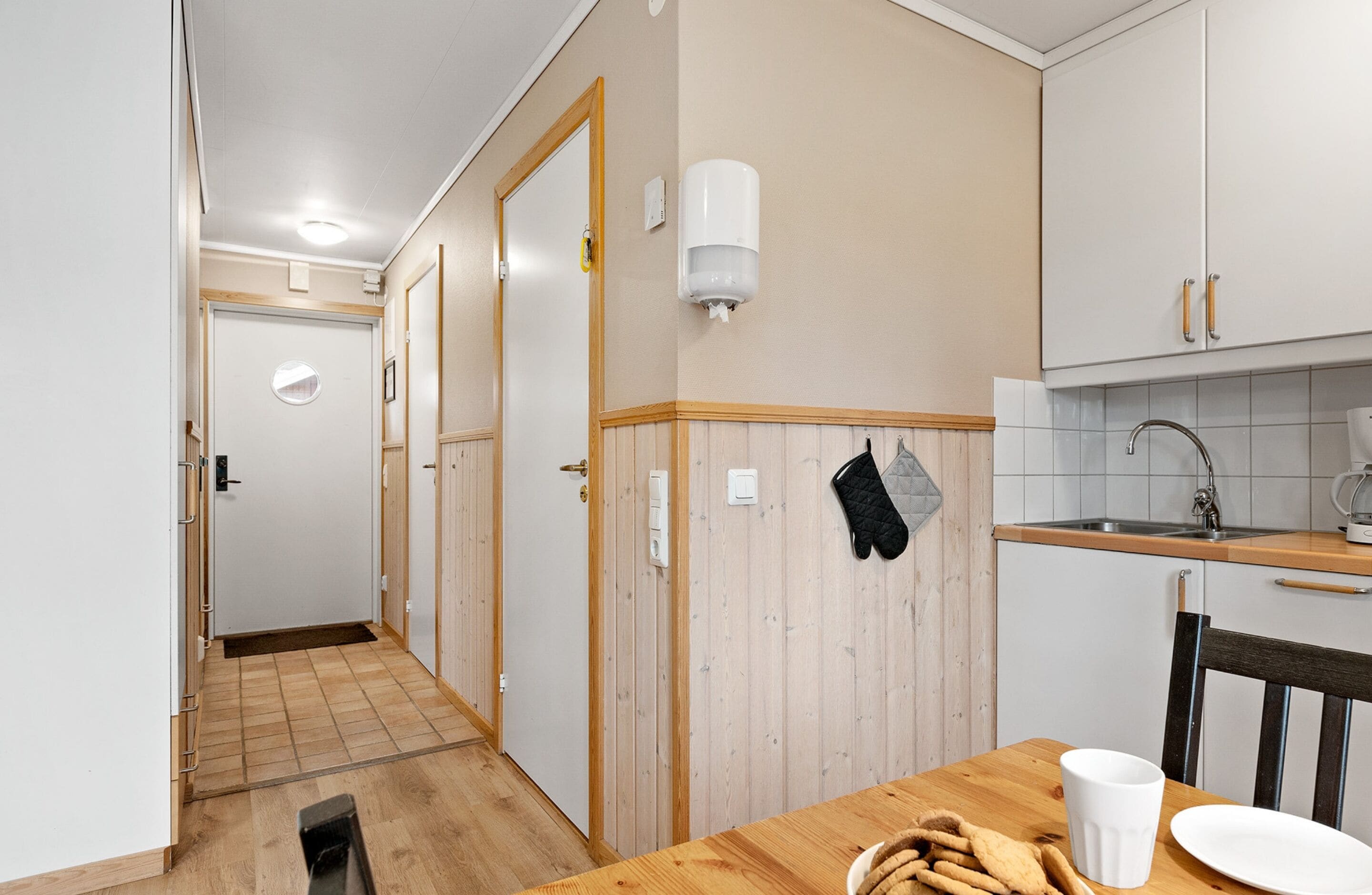 Un pasillo estrecho que conduce a una cocina con suelo de madera, un lavamanos y una ventana.