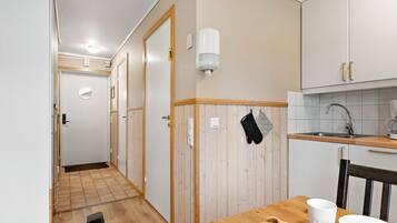 Un pasillo estrecho que conduce a una cocina con suelo de madera, un lavamanos y una ventana.