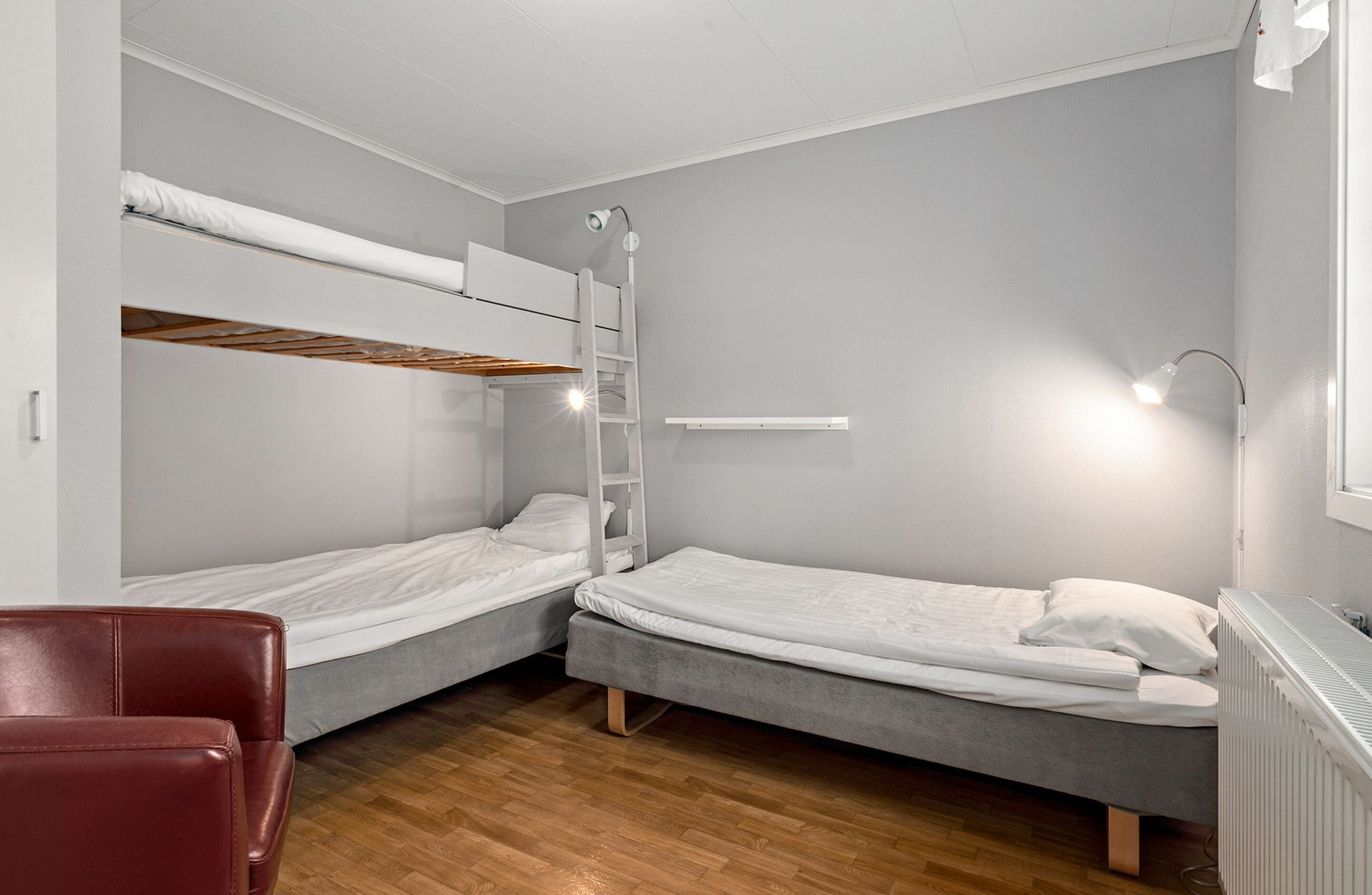 A small, modern room with two bunk beds, a red chair, and a radiator.