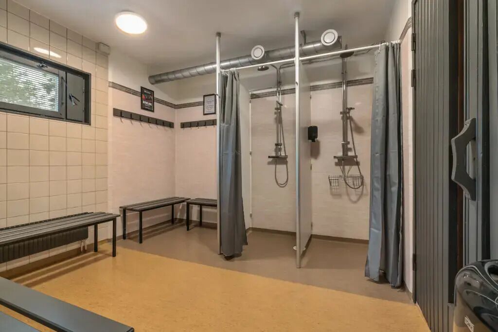 Baño público con zona de ducha, bancos y ventana.