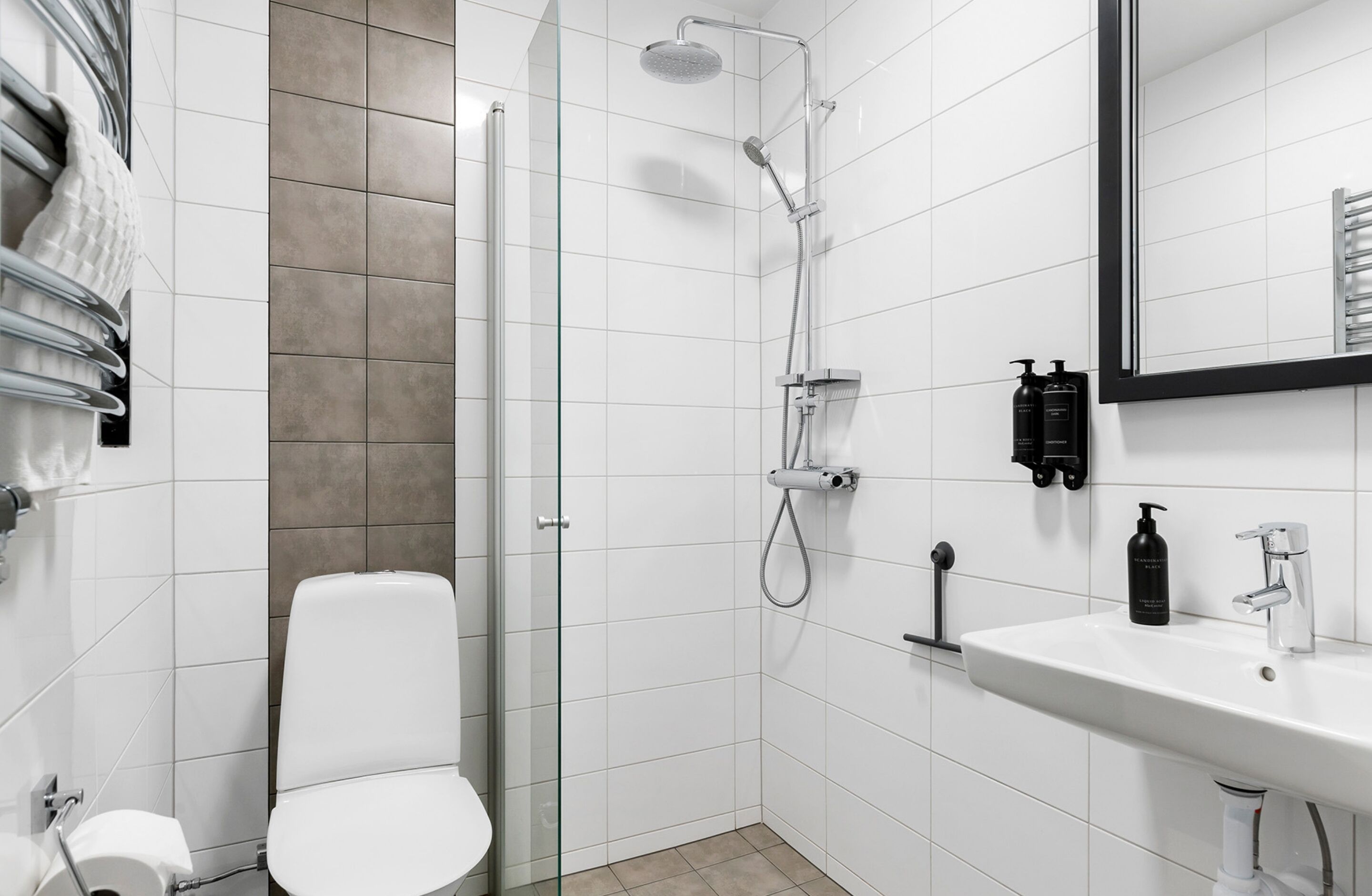 A modern bathroom with a glass shower enclosure, a white toilet, a sink with a mirror, and toiletries on the wall.