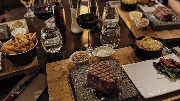 Mesa de jantar posta com diversos pratos, incluindo bife, batatas fritas e uma sobremesa, em um restaurante.