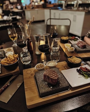 Ett matbord dukat med olika rätter, inklusive biff, pommes frites och en dessert, i en restaurangmiljö.