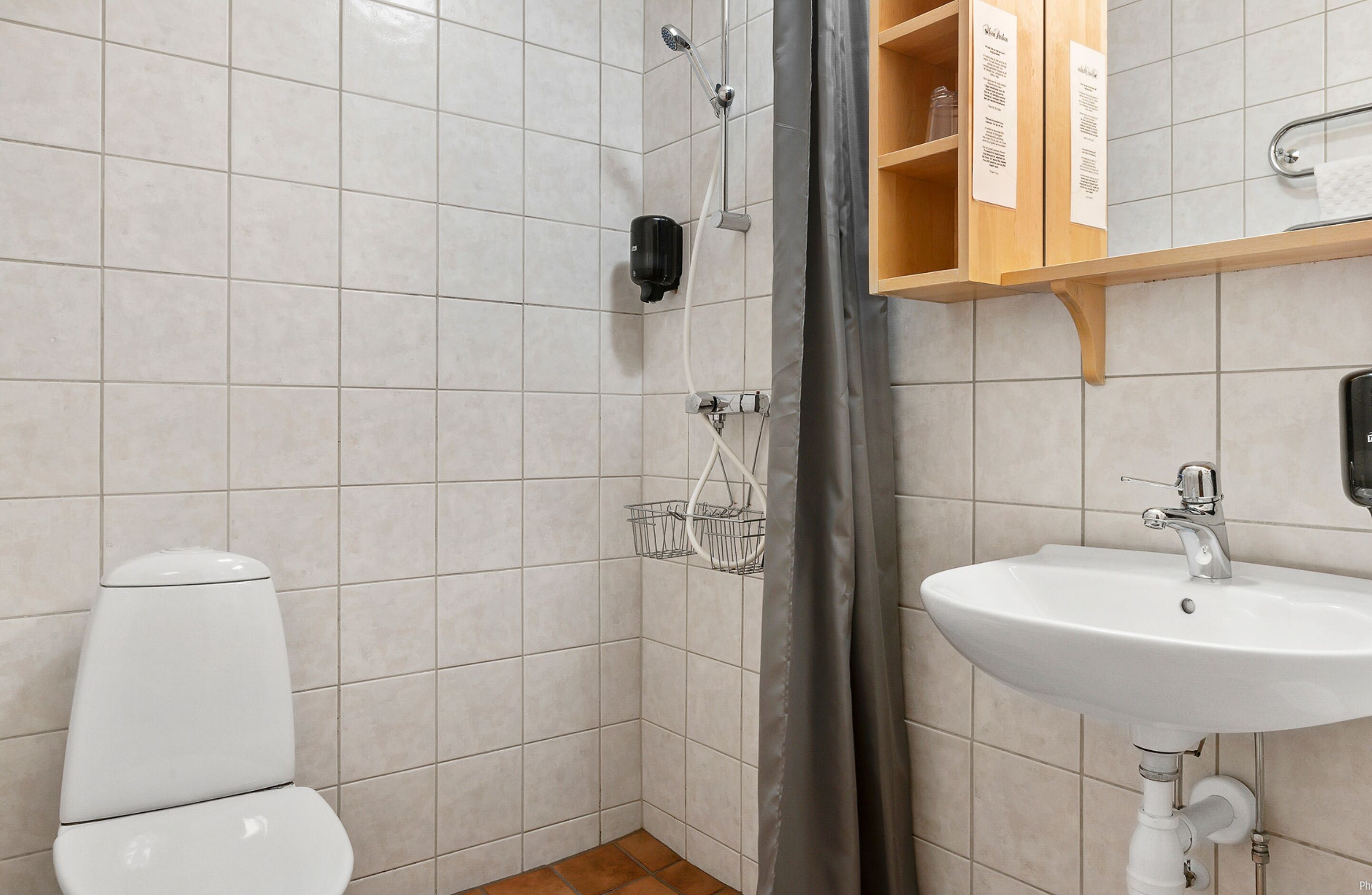 A bathroom with a toilet, a sink, a shower with a handheld showerhead, and a towel rack.