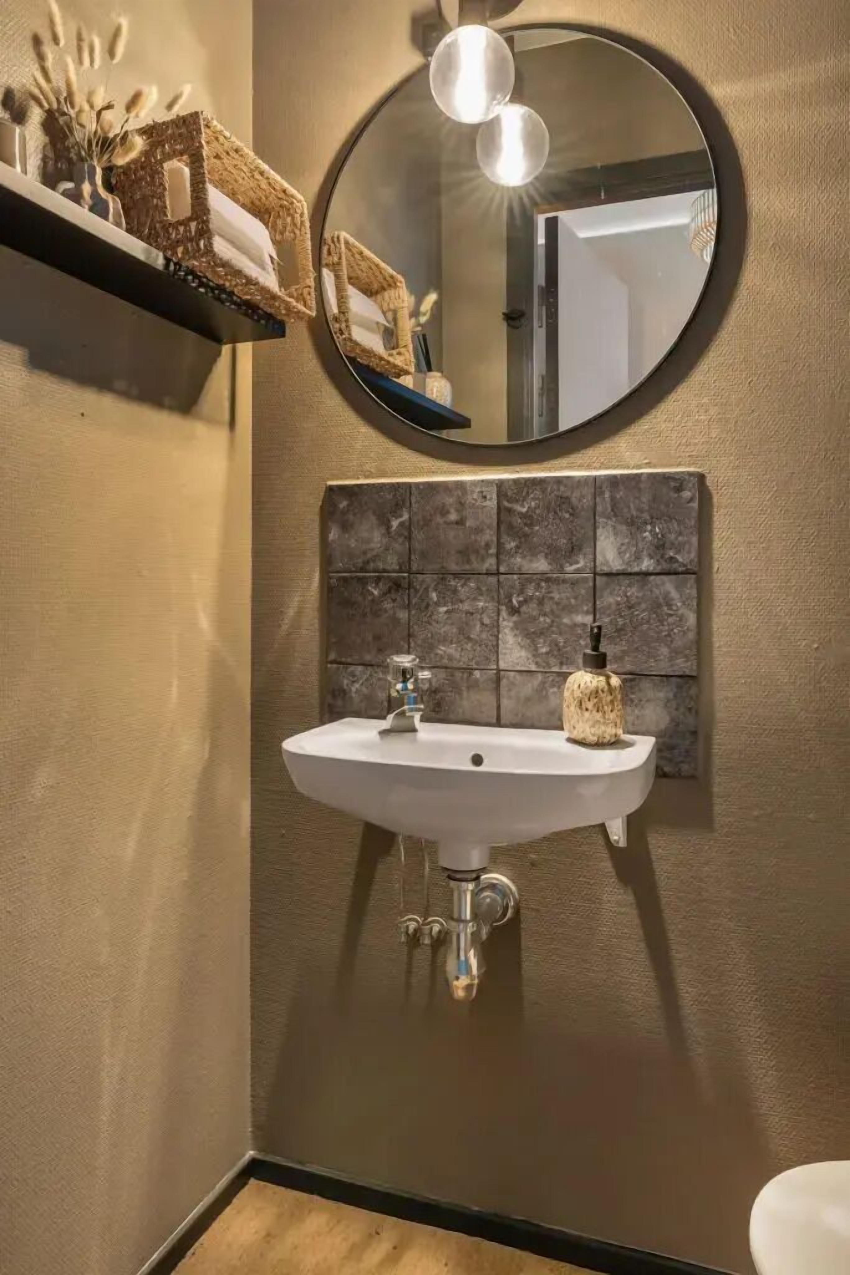 Ein Badezimmer mit einem weißen Waschbecken, einem runden Spiegel und einer Wandverkleidung mit Struktur.
