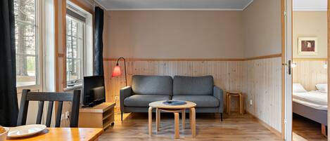 A cozy room with a sofa, a small round table, a TV, and a bed.