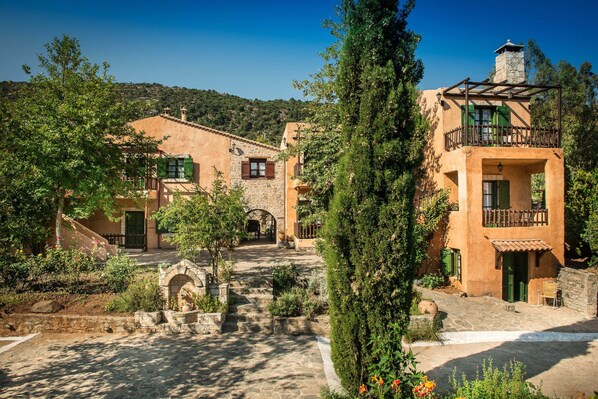 A traditional Mediterranean-style courtyard with stone pathways, rustic buildings, and lush greenery. - Enagron Cretan Ecotourism Village (Mylopotamos)