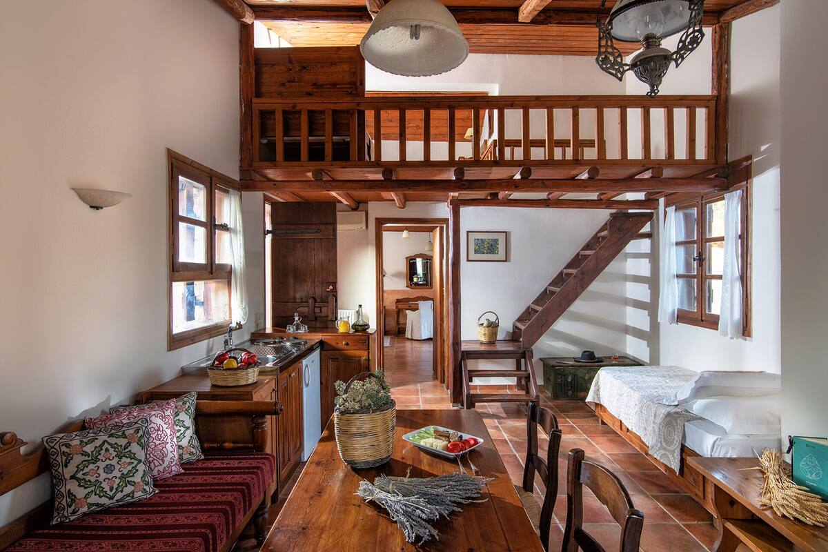 Een ruime loft met een houten trap, een eethoek en een gezellige zithoek met een bank en tafel.