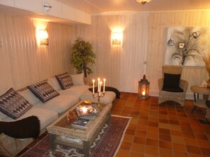 A cozy living room with a sofa, a coffee table with candles, a potted plant, and a wall-mounted light fixture. - Nya Pallas Hotel (Falkenberg)