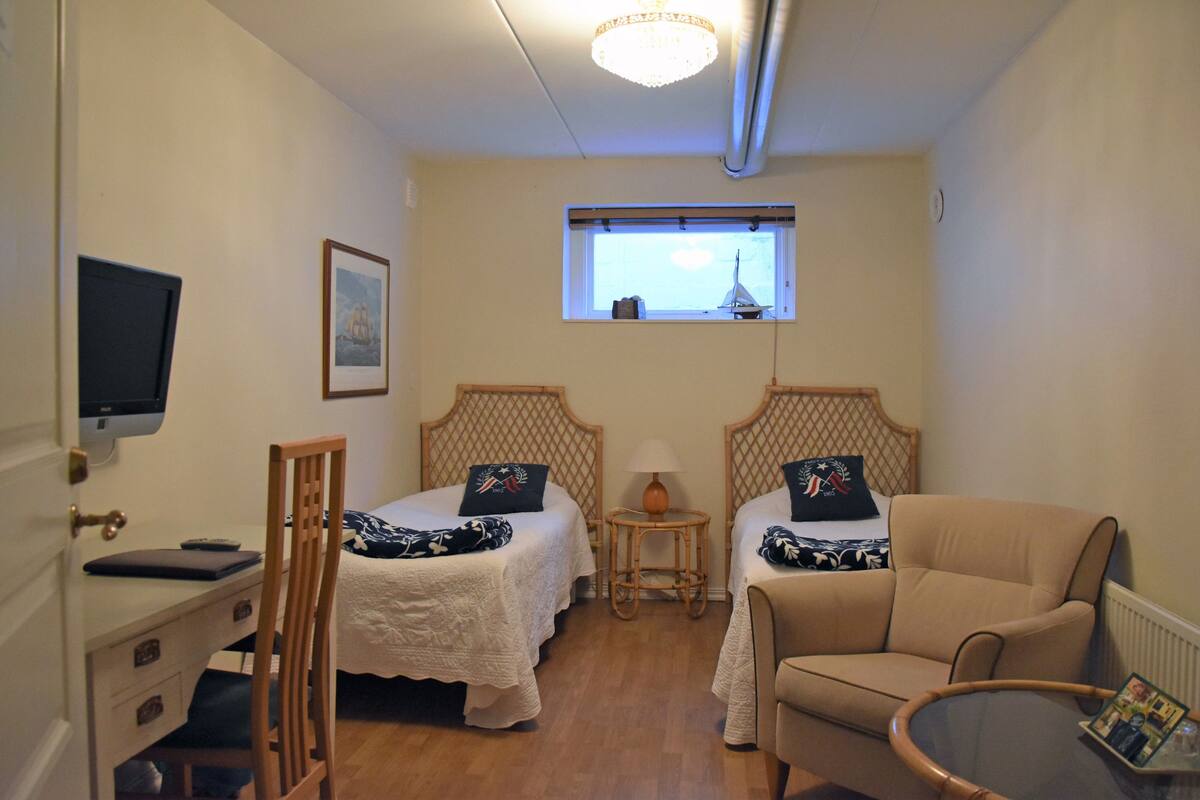 A bedroom with two beds, a desk, a chair, a lamp, and a window with a view.