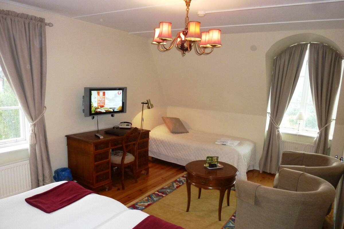 A hotel room with two beds, a desk with a chair, a television, and a chandelier.