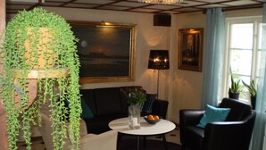 A living room with a round table, two armchairs, a sofa, a chandelier, and a large painting on the wall. - Nya Pallas Hotel (Falkenberg)