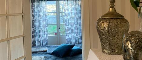 A room with a bed, a decorative vase, and a view through a door.