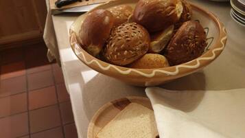 A breakfast buffet with various breads, rolls, and sliced white bread on a counter.