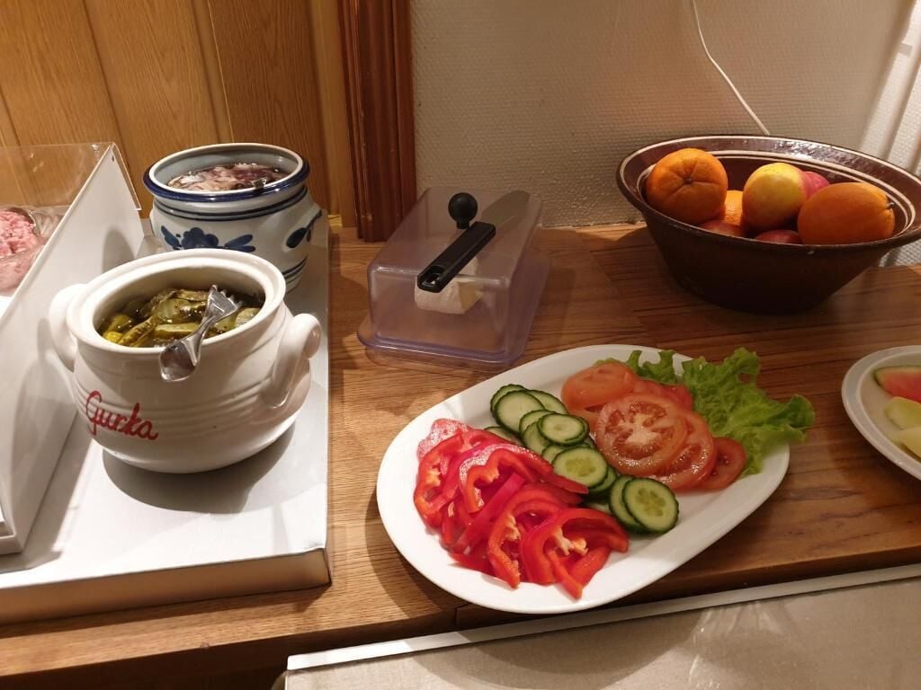 En köksbänk med en vit tallrik med skivad grönsallad, en skål med apelsiner, en burk inlagda grönsaker och en vit mugg med texten "Gupta".