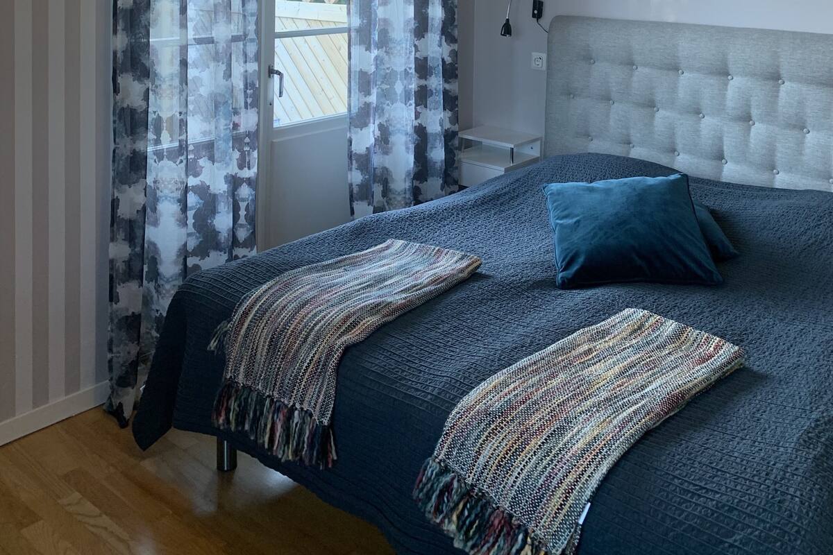 A bedroom with a large bed, a headboard, a ceiling light, and a window with curtains.