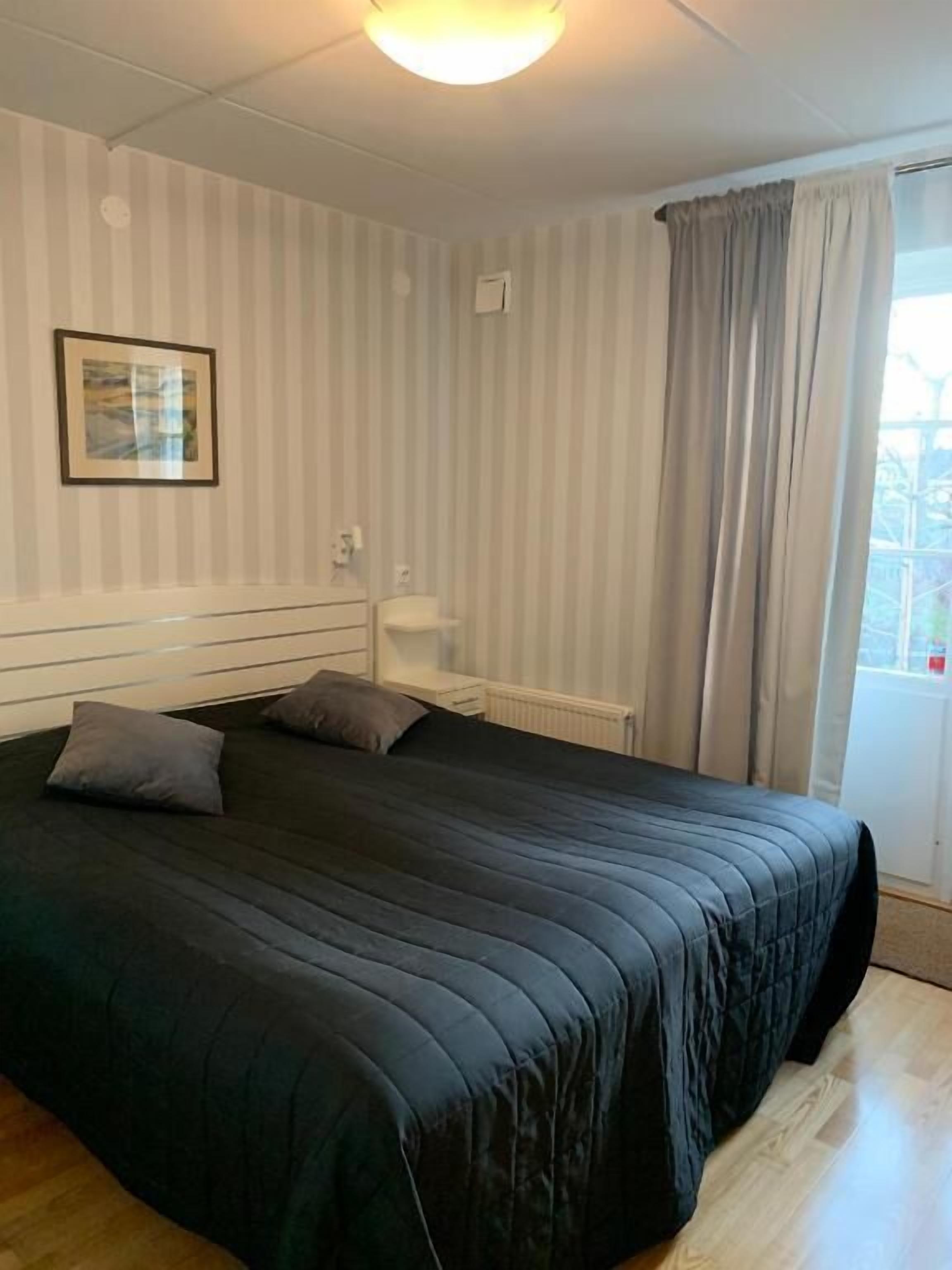 A bedroom with a large bed, a bedside table, a radiator, and a window with curtains.