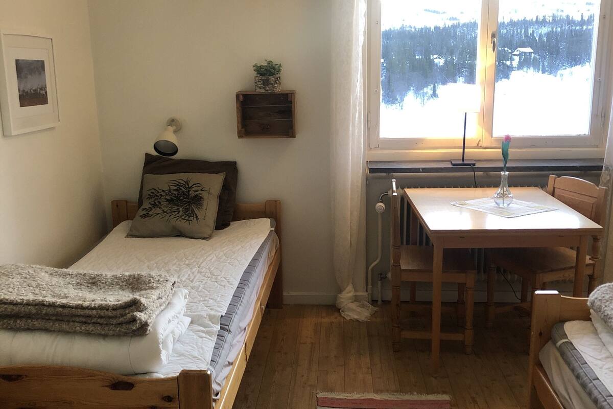 Une pièce confortable avec un lit, une petite table et une fenêtre donnant sur un paysage enneigé.