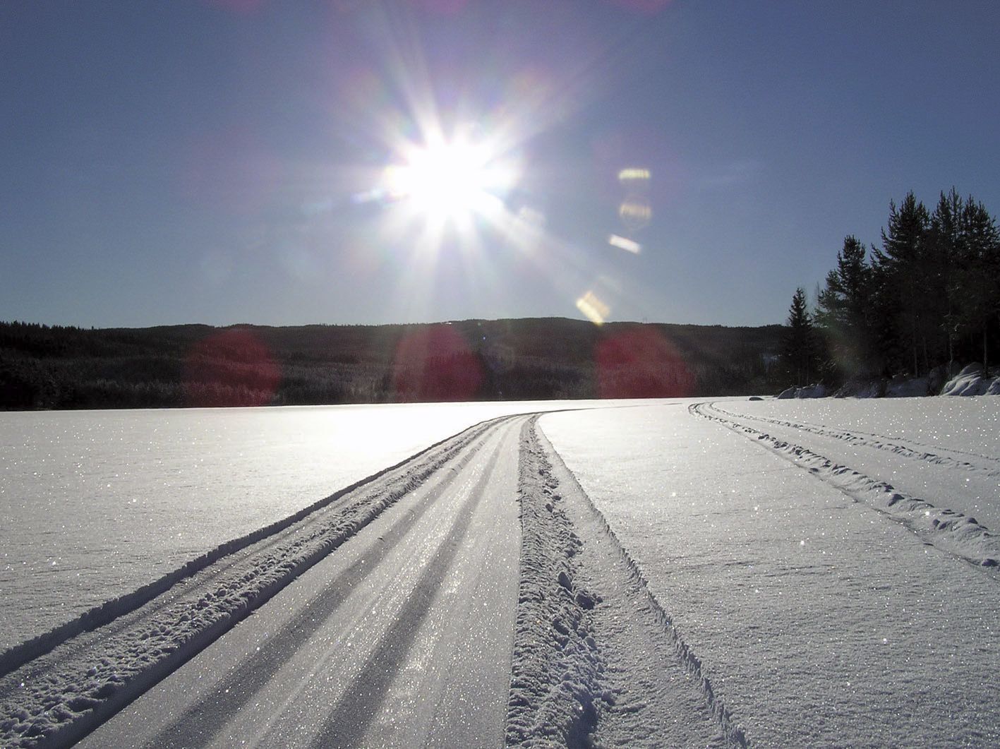 A snowy landscape with a clear sky and a bright sun.
