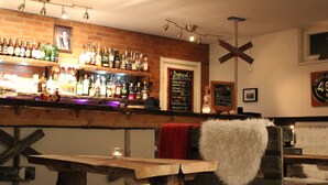 Eine Bar mit Backsteinwand, Flaschenregalen, einer Kreidetafel mit Speisekarte und rustikalen Holmöbeln.