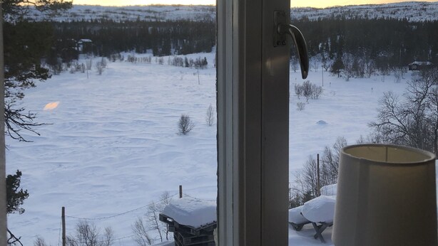 Blick durch ein Fenster auf eine verschneite Landschaft, auf dem Fensterbrett steht eine Lampe.