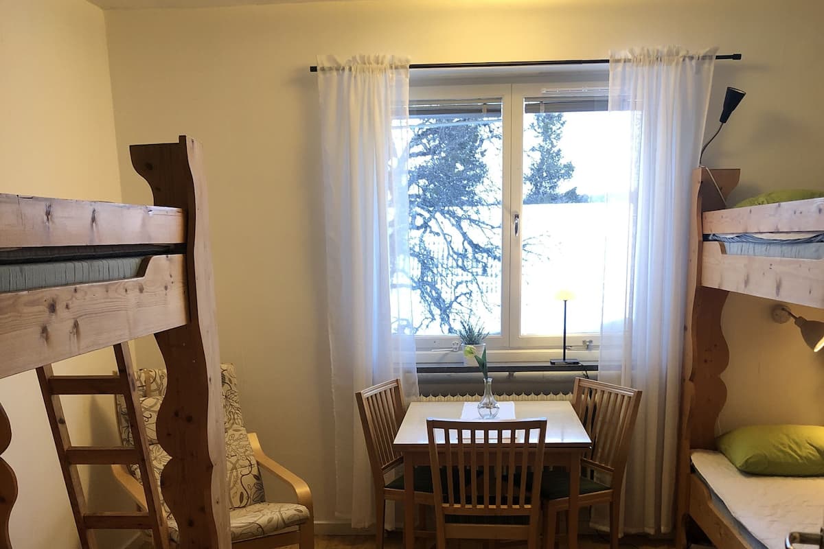 Une pièce confortable avec des lits superposés, une table à manger avec des chaises, une fenêtre avec des rideaux et une petite table avec une lampe.