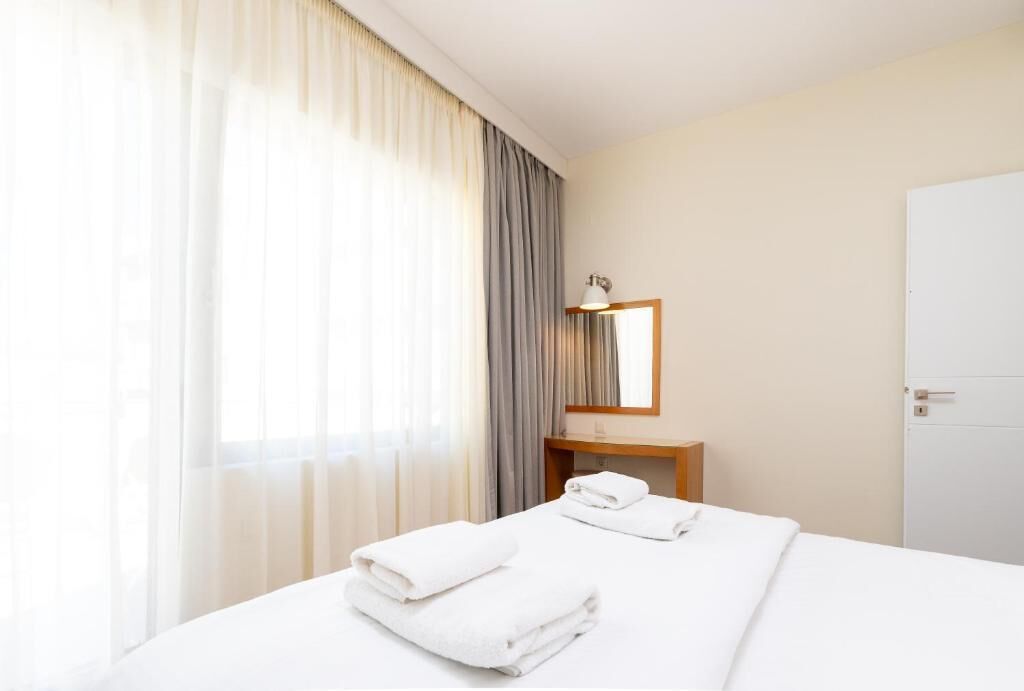 Quarto de hotel com uma cama, mesa de cabeceira, espelho e porta.