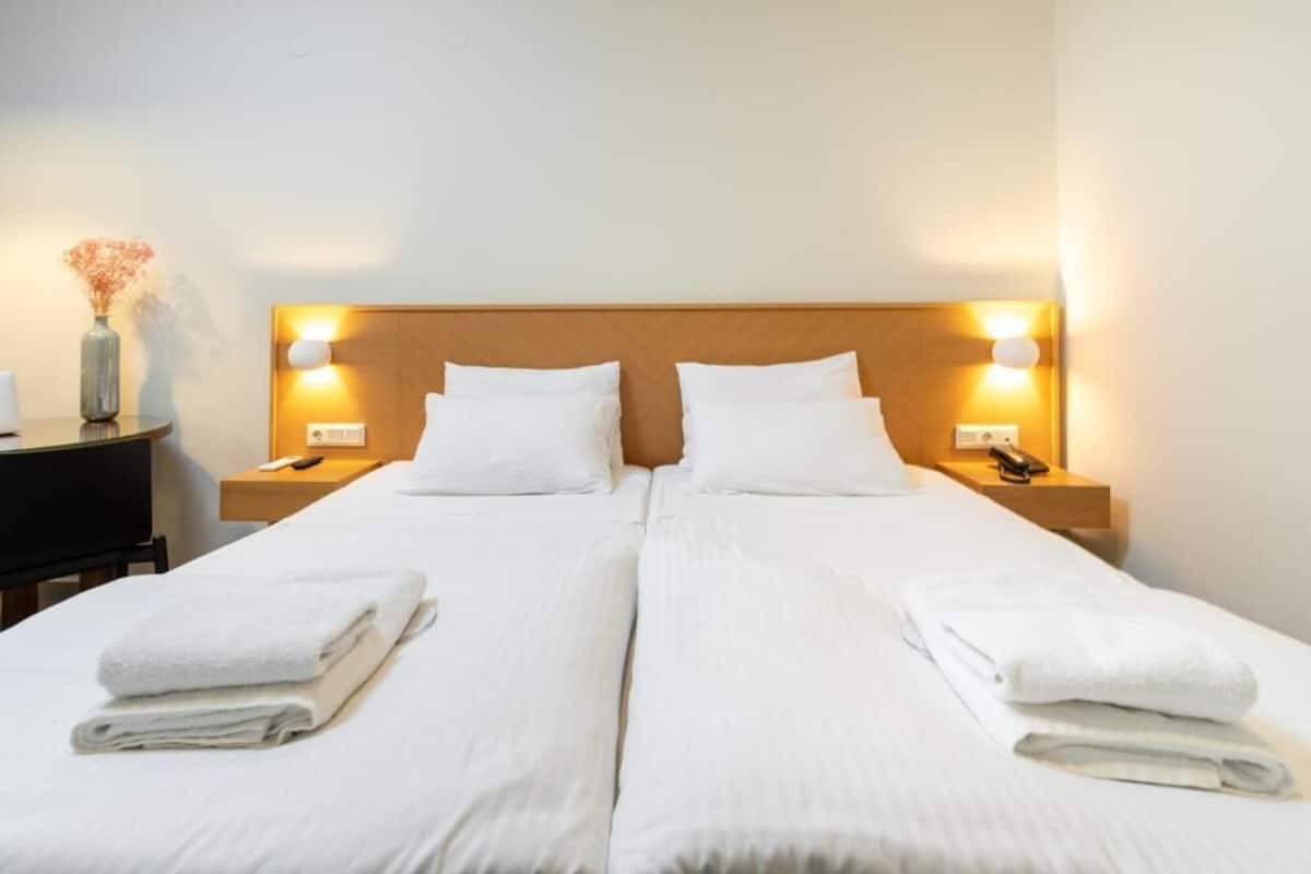 A double bed with white linens and two bedside tables with lamps.