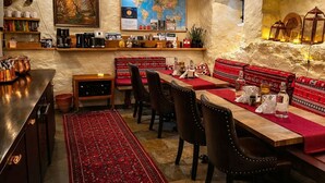 A cozy restaurant with a rustic interior, featuring a long wooden table set for dining, a red patterned rug, and a world map on the wall.