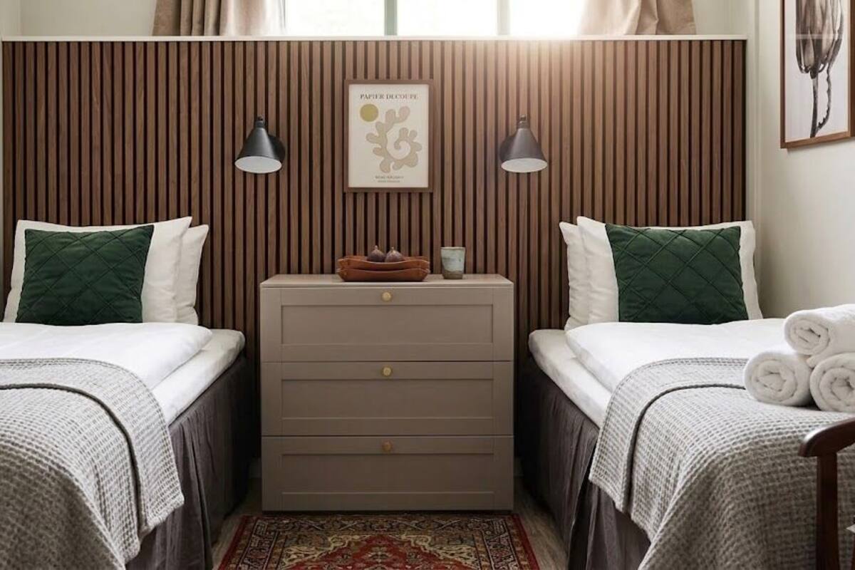 Hotellihuone, jossa on kaksi sänkyä, yöpöytä, kehystetty kuva ja pieni pöytä, jonka pääll ä on kynttilä.